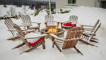 Backyard patio with fire pit and Adirondack chairs covered in snow.