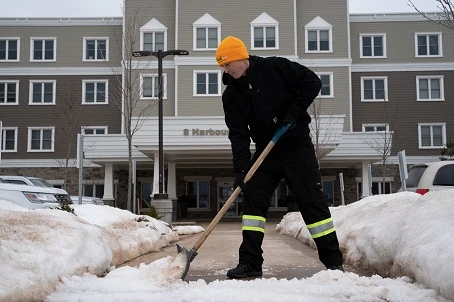 Grounds Guys service professional shoveling snow in front of apartment building.