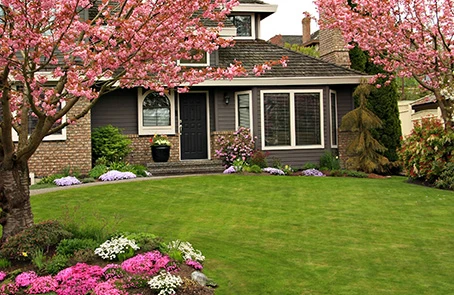 Single-family home with well-manicured front lawn, flowering crabapple trees, shrubs, and flower beds.