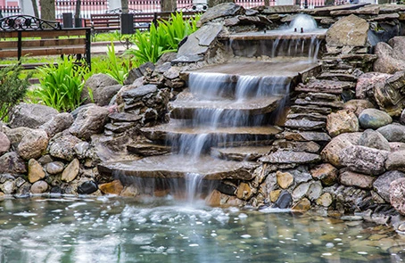 Artificial waterfall cascading down rocks into a pond in a city park.