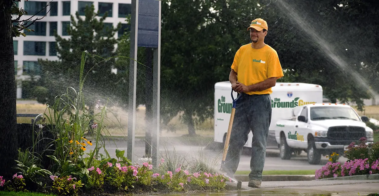 The Grounds Guys service professional monitoring a sprinkler system as it sprays water on a lawn.