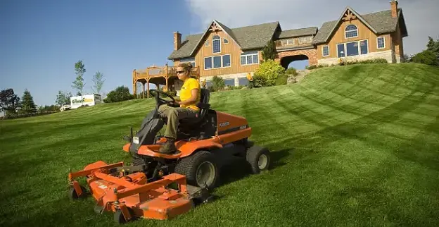 The Grounds Guys service professional mowing a large home's front lawn.