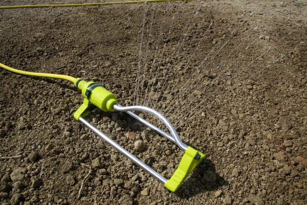 Sprinkler watering soil with grass seeds