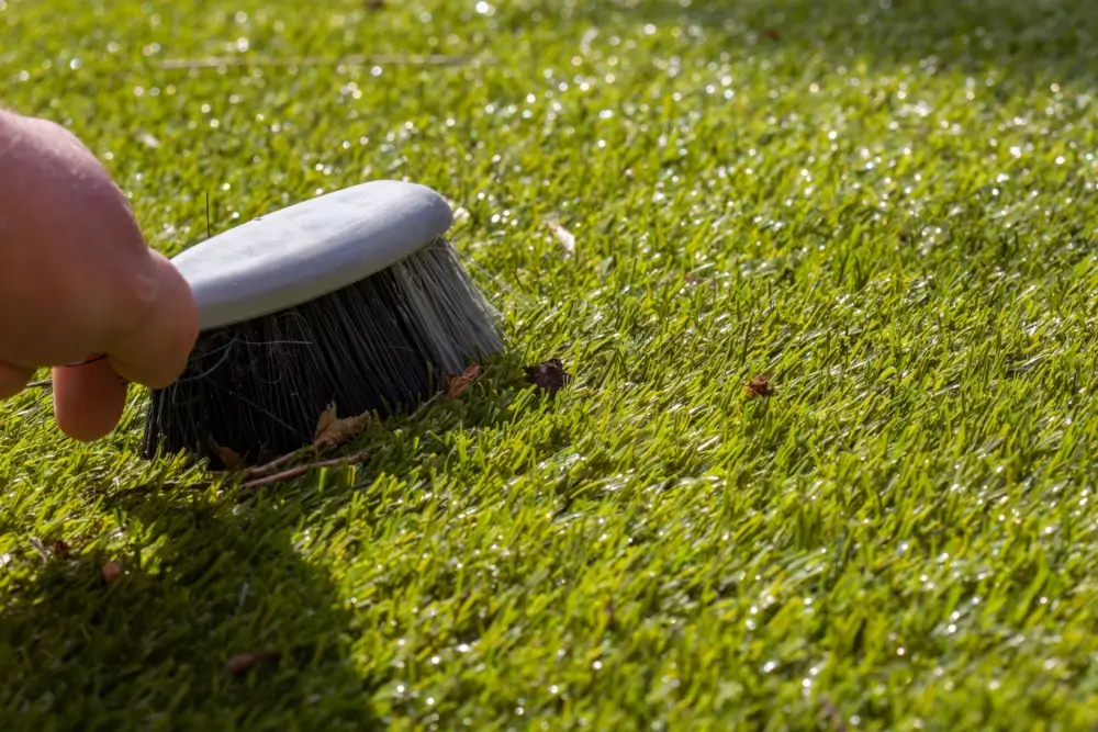 Man brushing artifiicial grass turf with a hand brush.