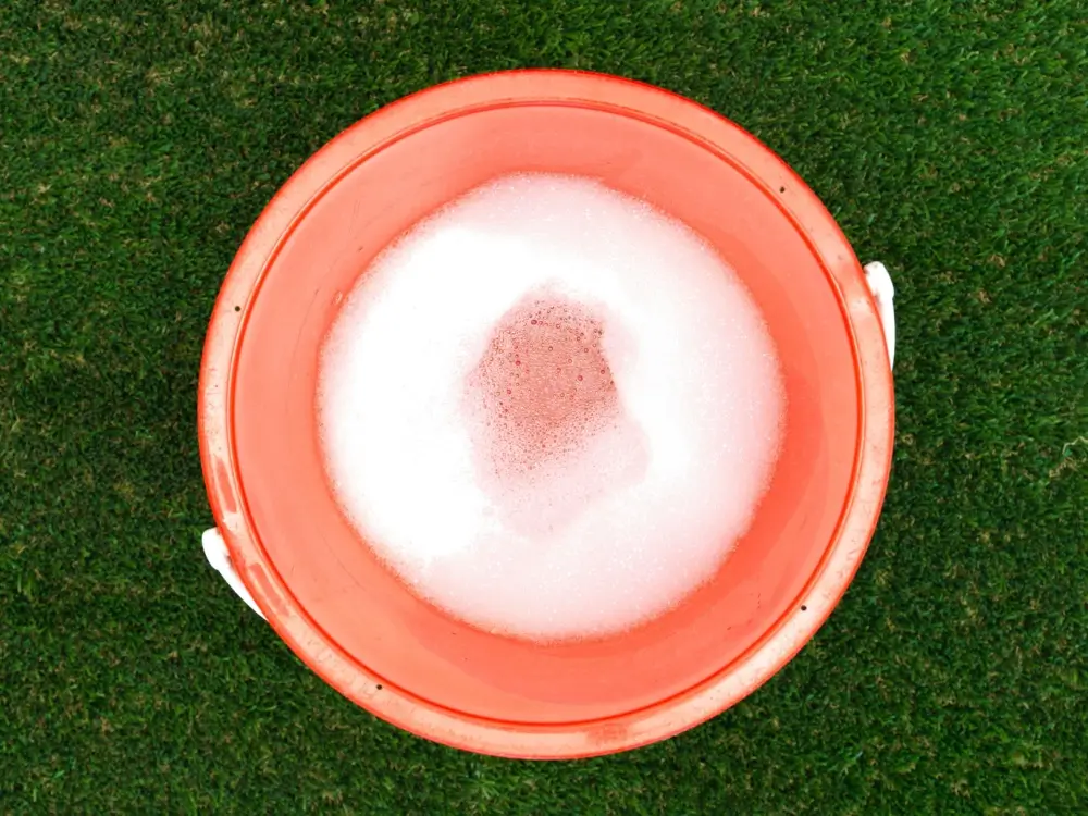 Bucket of soap and water on artificial turf.