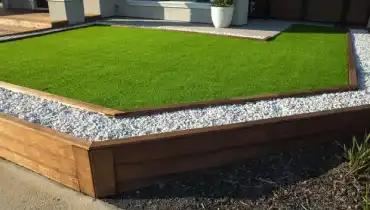 Small artificial turf lawn with rock-bed edge in front yard of home.