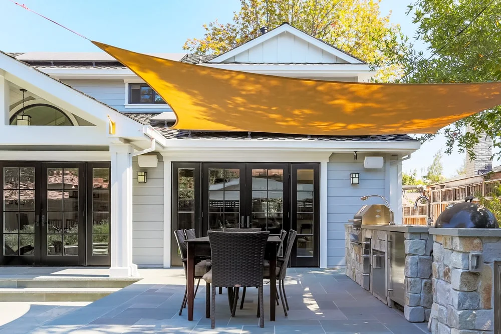Yellow canopy covering table, chairs, and grill in backyard patio area of a residential home