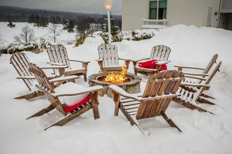 Backyard patio with fire pit and Adirondack chairs covered in snow.