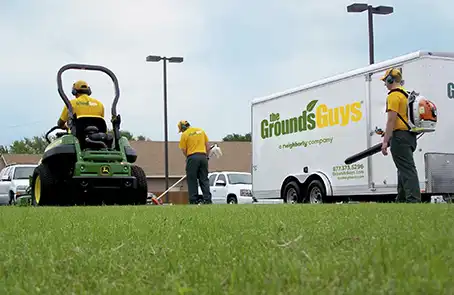 Three Grounds Guys employees performing lawn cleanup next to a branded company trailer.