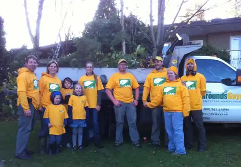 The Grounds Guys of Abbotsford team smiling and wearing yellow shirts while standing in front of Grounds Guys truck.