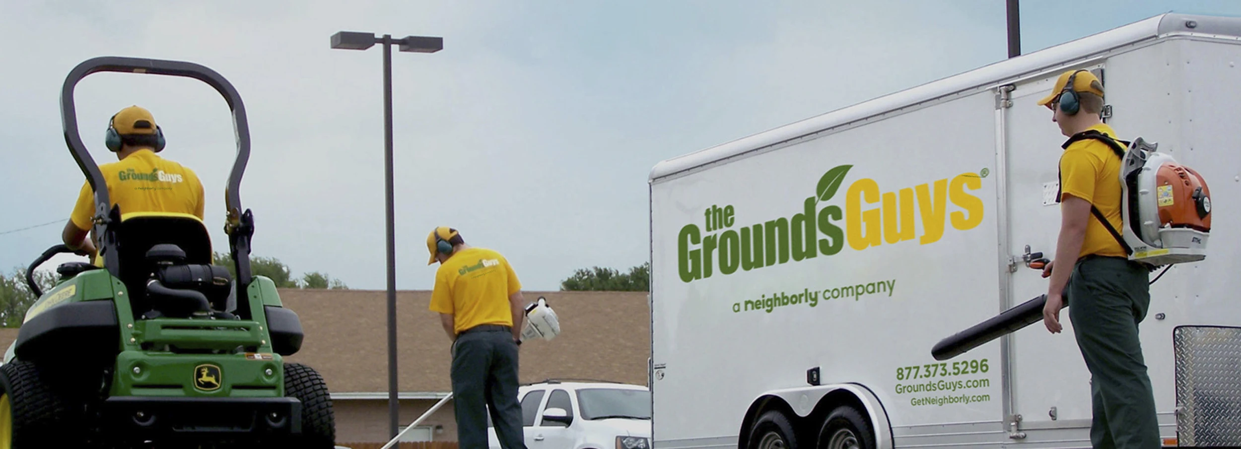 Three Grounds Guys employees performing lawn cleanup work next to a branded company trailer.