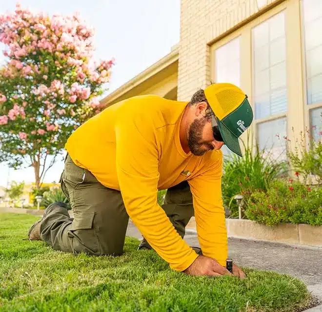 The Grounds Guys service professional adjusting a sprinkler embedded in grass.