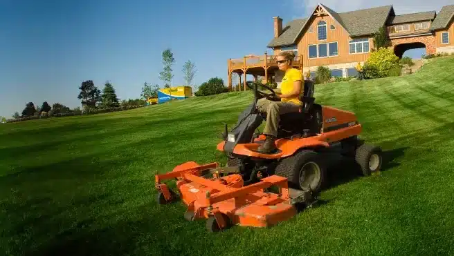 The Grounds Guys service professional mowing a large home's front lawn.