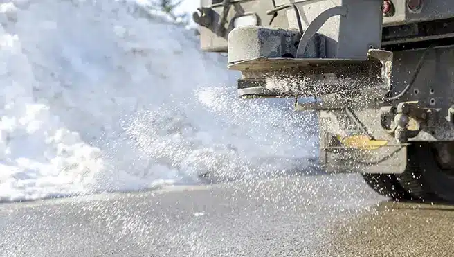 Salt spraying from the back of a truck as it salts a snowy road.