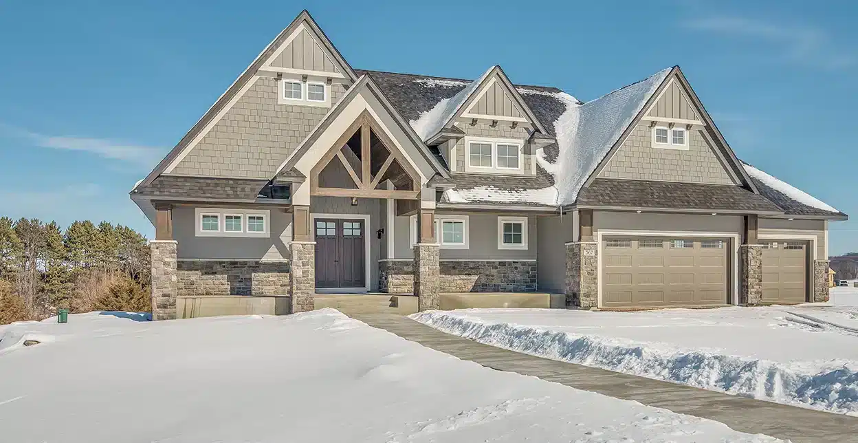 Snow-covered driveway and walkway cleared in front of a two-story suburban home.